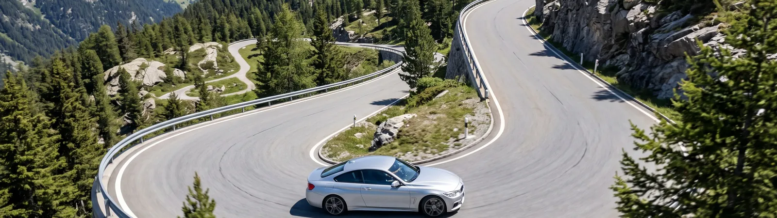 Deportivo plateado en una curva de una carretera de montaña soleada